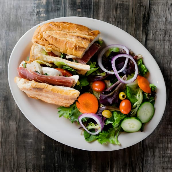 Piu Bello Buckhead's prosciutto and mozzarella sandwich with a side salad on a white plate.