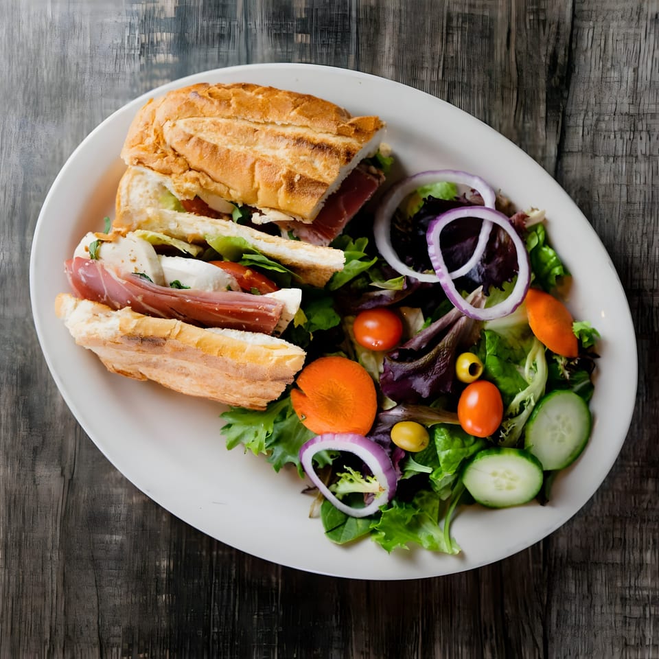 Piu Bello Buckhead's prosciutto and mozzarella sandwich with a side salad on a white plate.